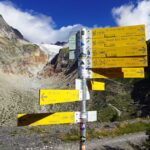 Cartelli segnavia al Rifugio Elena (2066 m), in Val Ferret, con il ghiacciaio di Pré de Bar sullo sfondo.